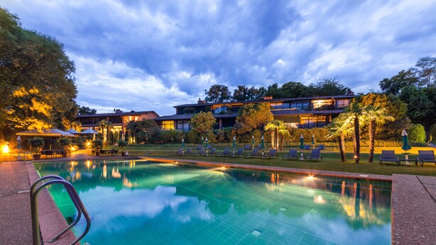 A swimming pool with lounge chairs and umbrellas, surrounded by trees and buildings. - Park Hotel Principe (Collina d'Oro)