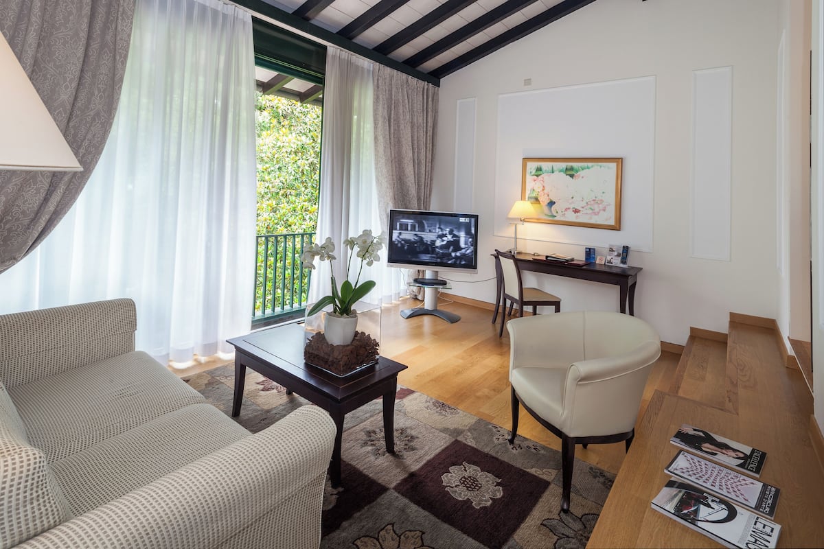 A living room with a sofa, armchair, coffee table, TV, and a painting on the wall.