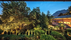 A modern building with a glass facade, surrounded by dense greenery and a mountain in the background. - Park Hotel Principe (Collina d'Oro)