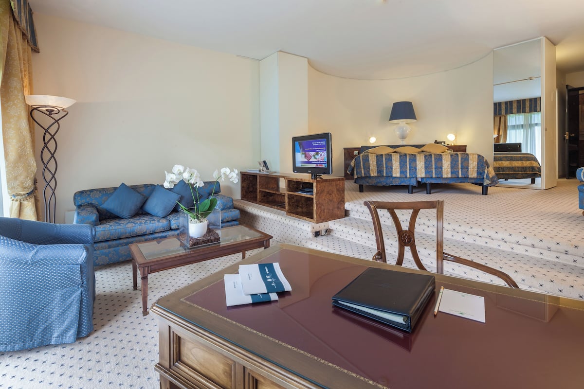 A hotel room with a sofa, a bed, a desk with a laptop, a TV, and a mirror.