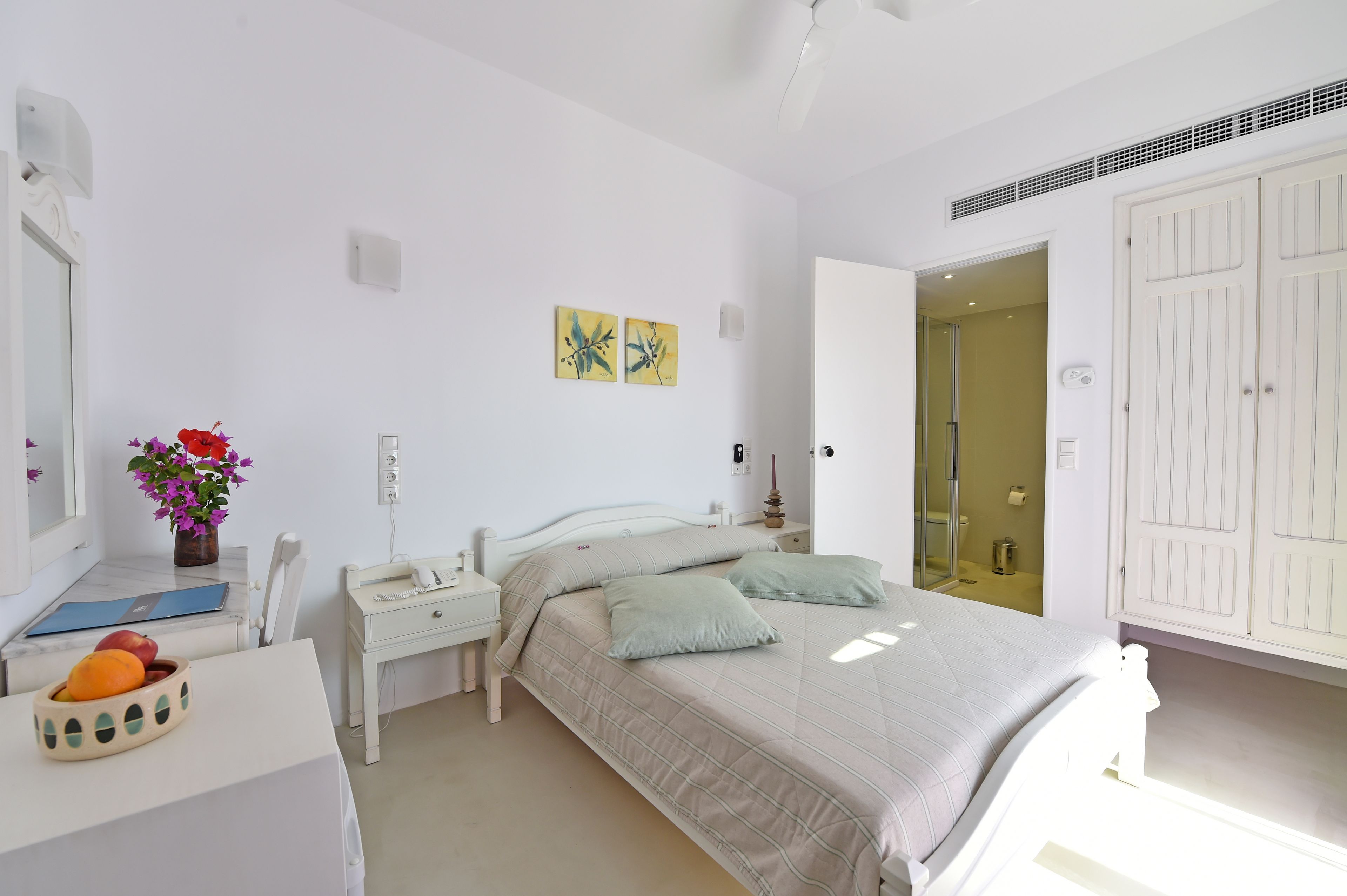 A bedroom with a bed, bedside tables, a mirror, a vase with flowers, and a door leading to a bathroom.