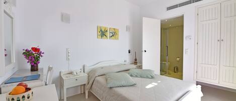 A bedroom with a bed, bedside tables, a mirror, a vase with flowers, and a door leading to a bathroom.