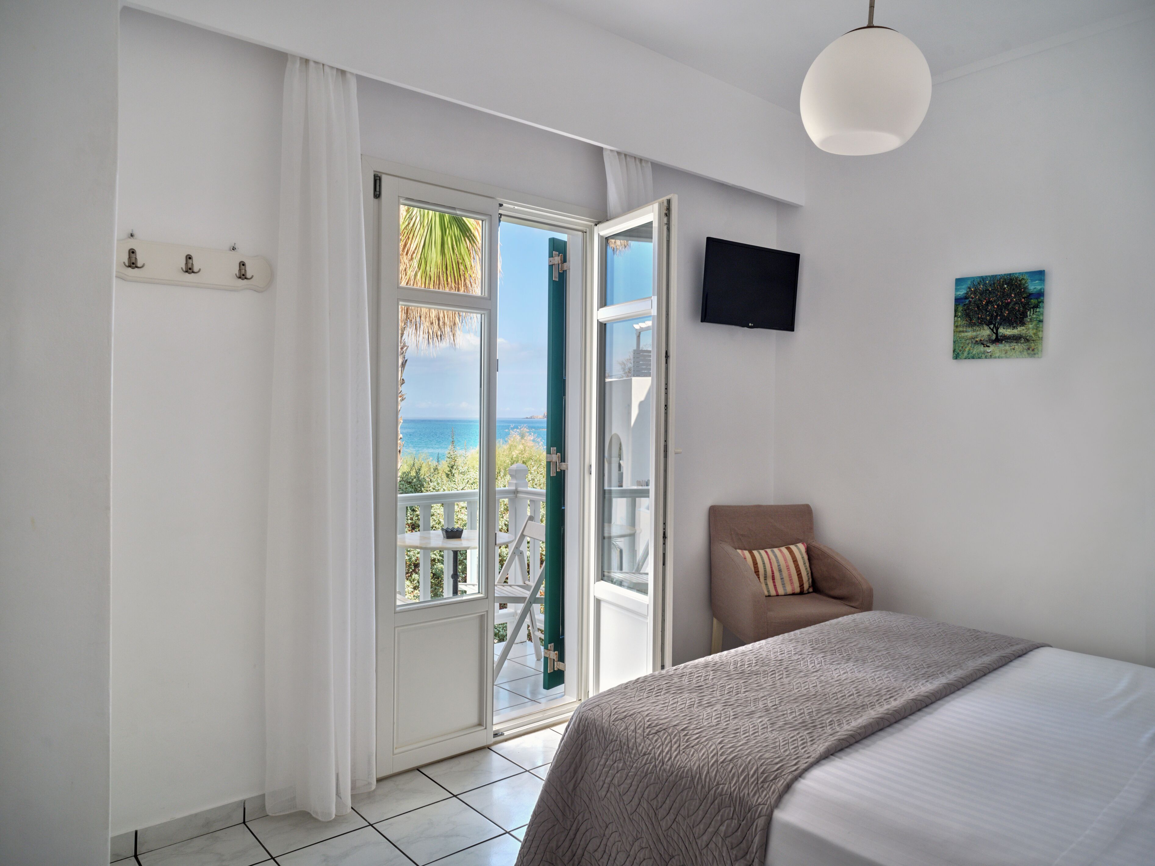 Quarto com cama, cadeira, TV e varanda com vista para o mar.