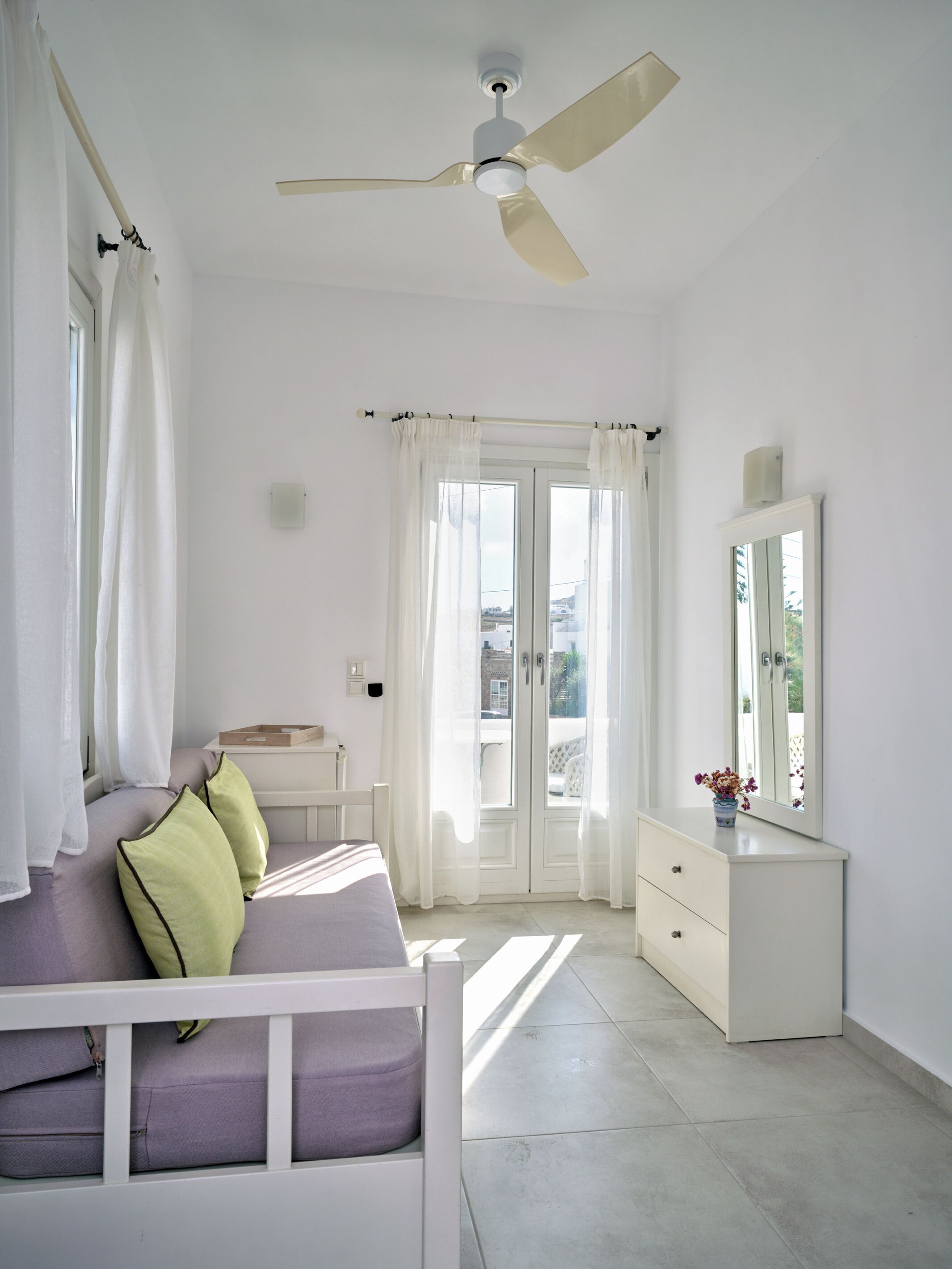 Una habitación luminosa con una cama, un tocador, un espejo y un ventilador de techo.