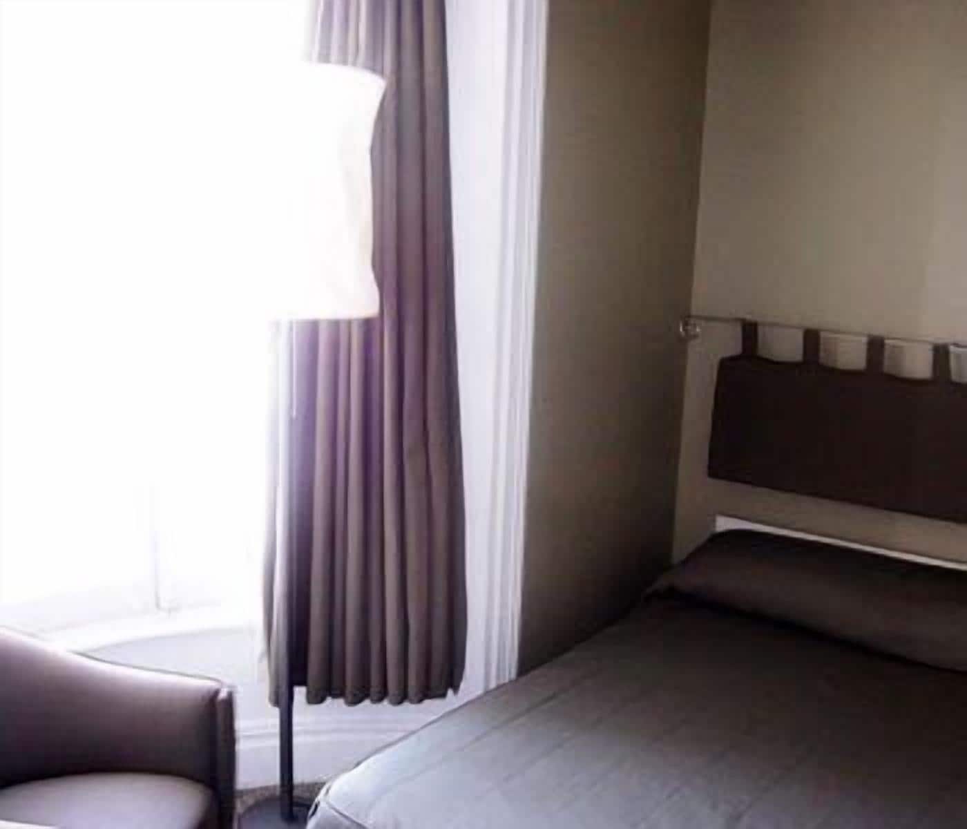 Een hotelkamer met een bed, een stoel en een raam met gordijnen.