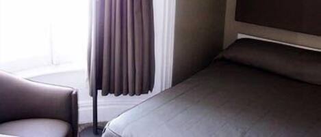 Habitación de hotel con cama, una silla y ventana con cortinas.