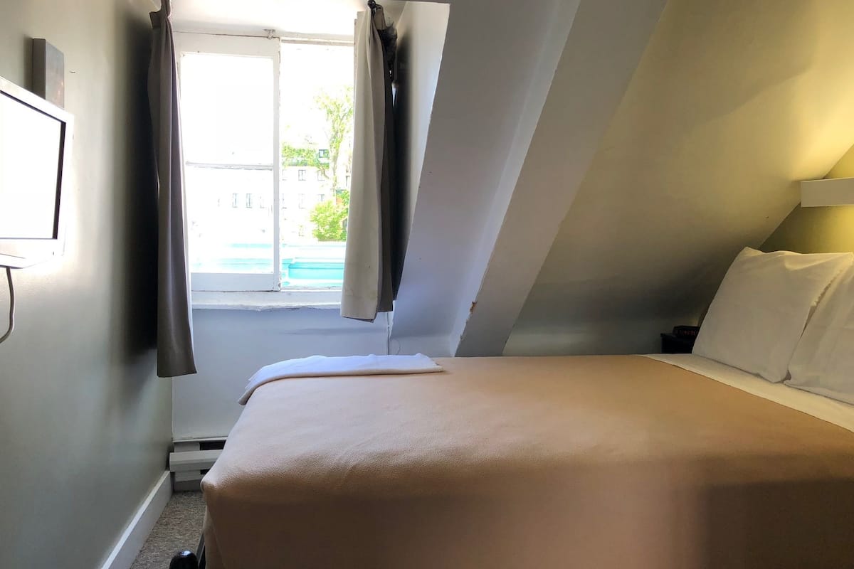 A bedroom with a bed, a nightstand, a window with curtains, and a view of a swimming pool.