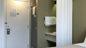 A hotel room with a bed, a bathroom with a shower, and an air conditioning unit.