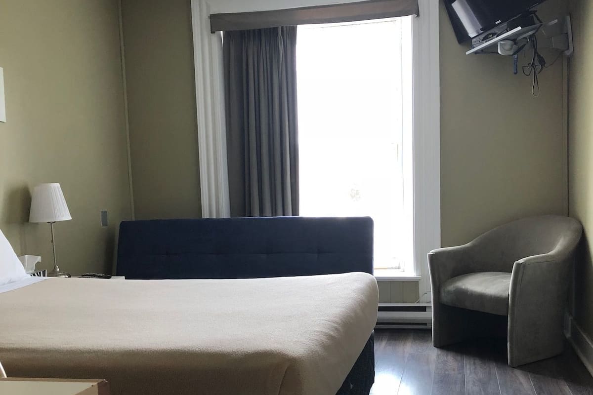 A hotel room with a bed, a chair, a TV, and a window with curtains.