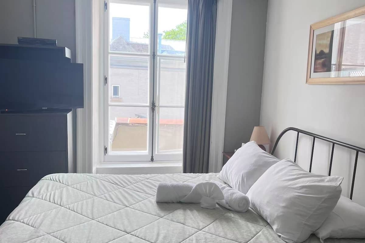 A hotel room with a bed, a dresser, a window with curtains, a lamp, and a framed picture on the wall.