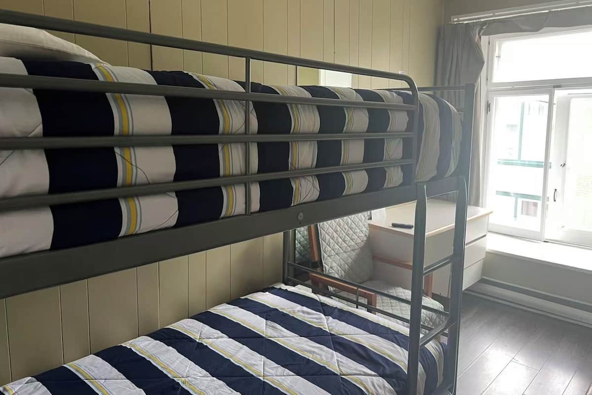 A bunk bed with striped bedding, a wooden headboard, a window with curtains, and a door leading outside.