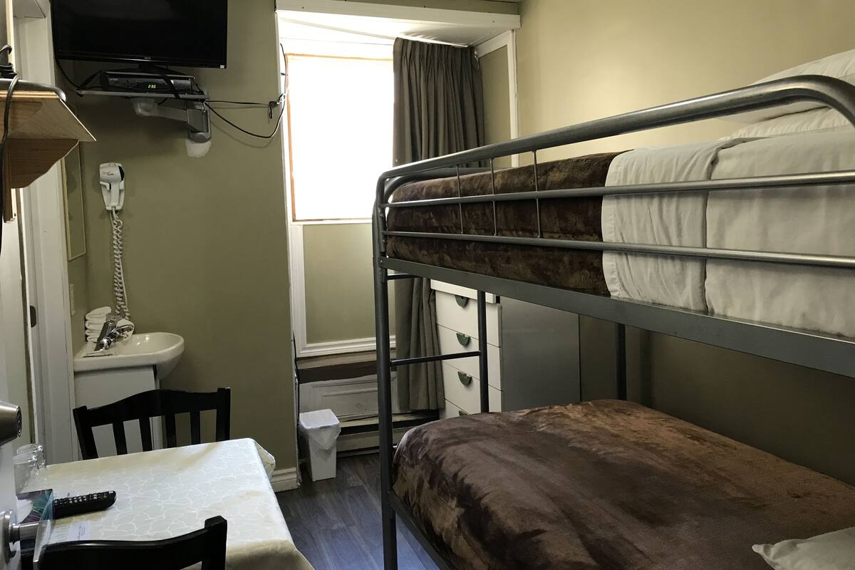 A bunk bed room with a television, a sink, and a window.