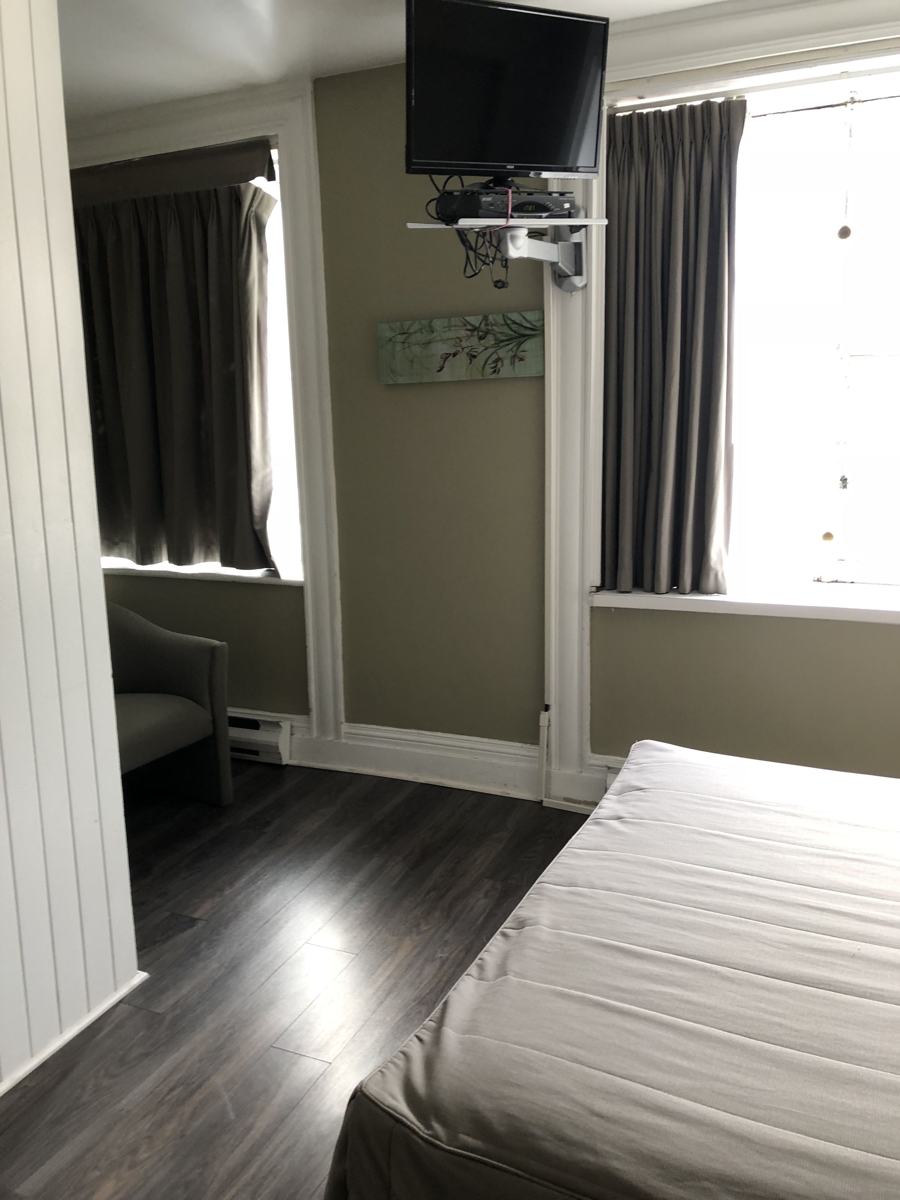 A bedroom with a bed, a TV mounted on the wall, a window with curtains, and a small table.