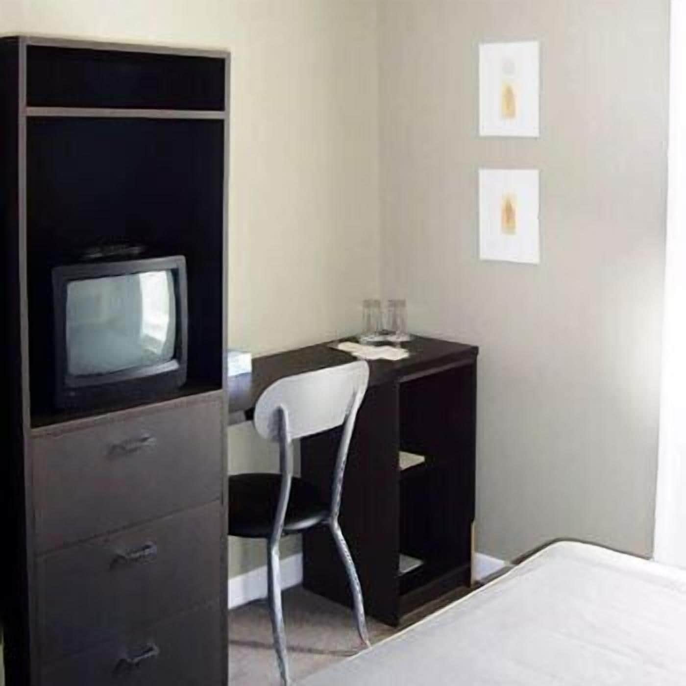 Une chambre d’hôtel avec un lit, un bureau et une chaise, un téléviseur posé sur un meuble, et deux tableaux encadrés accrochés au mur.