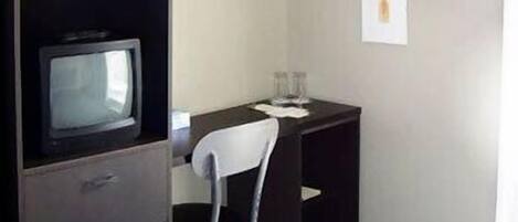 Une chambre d’hôtel avec un lit, un bureau et une chaise, un téléviseur posé sur un meuble, et deux tableaux encadrés accrochés au mur.