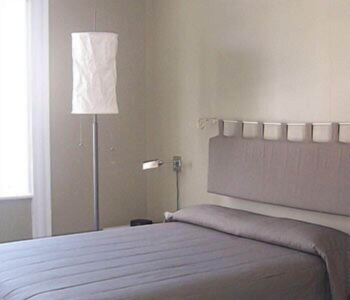 A bedroom with a bed, a bedside table, a lamp, and a wall-mounted light fixture.