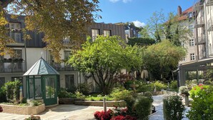 A courtyard with a green gazebo, a fountain, and a variety of plants and flowers. - MAXIMILIAN MUNICH Apartments & Hotel  (Munich)