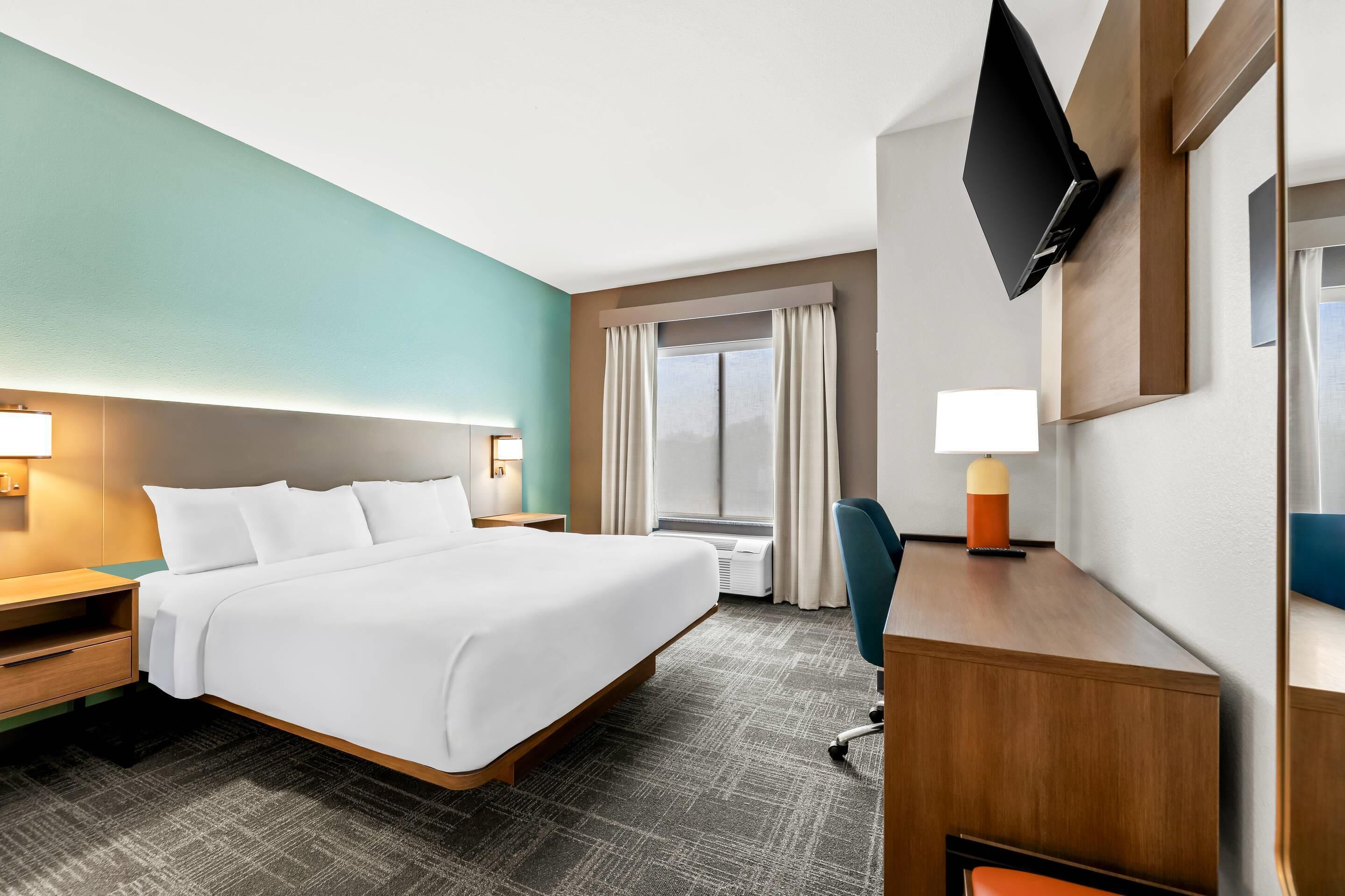 Habitación de hotel con una cama grande, un escritorio con silla, un televisor de pantalla plana y una ventana con cortinas.