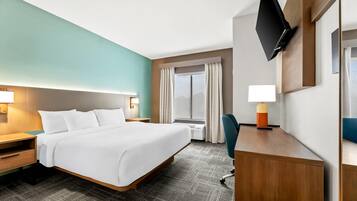 Quarto de hotel com uma cama grande, uma escrivaninha com cadeira, uma televisão de tela plana e uma janela com cortinas.