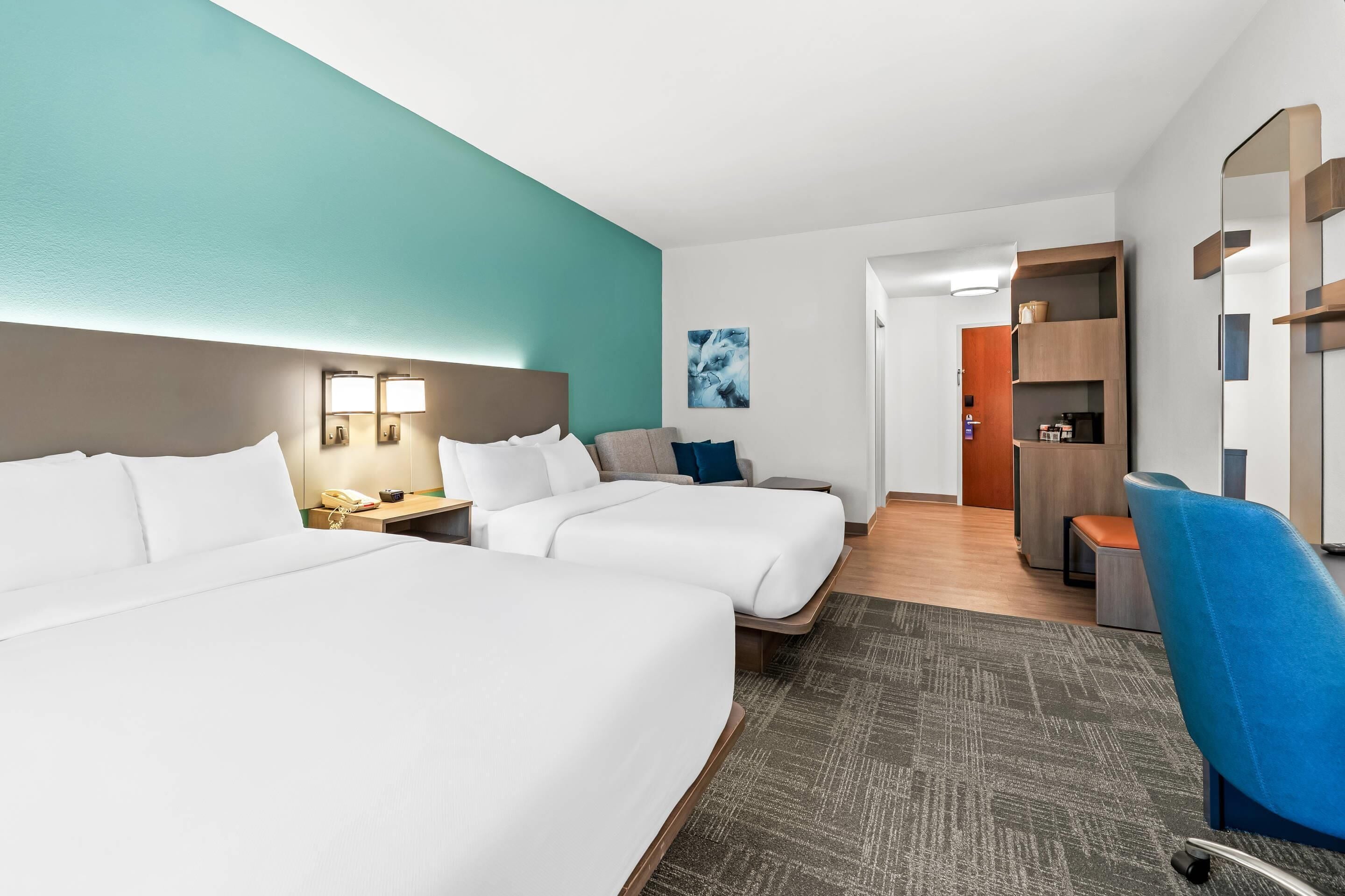 A hotel room with two beds, a desk, a chair, and a mirror.