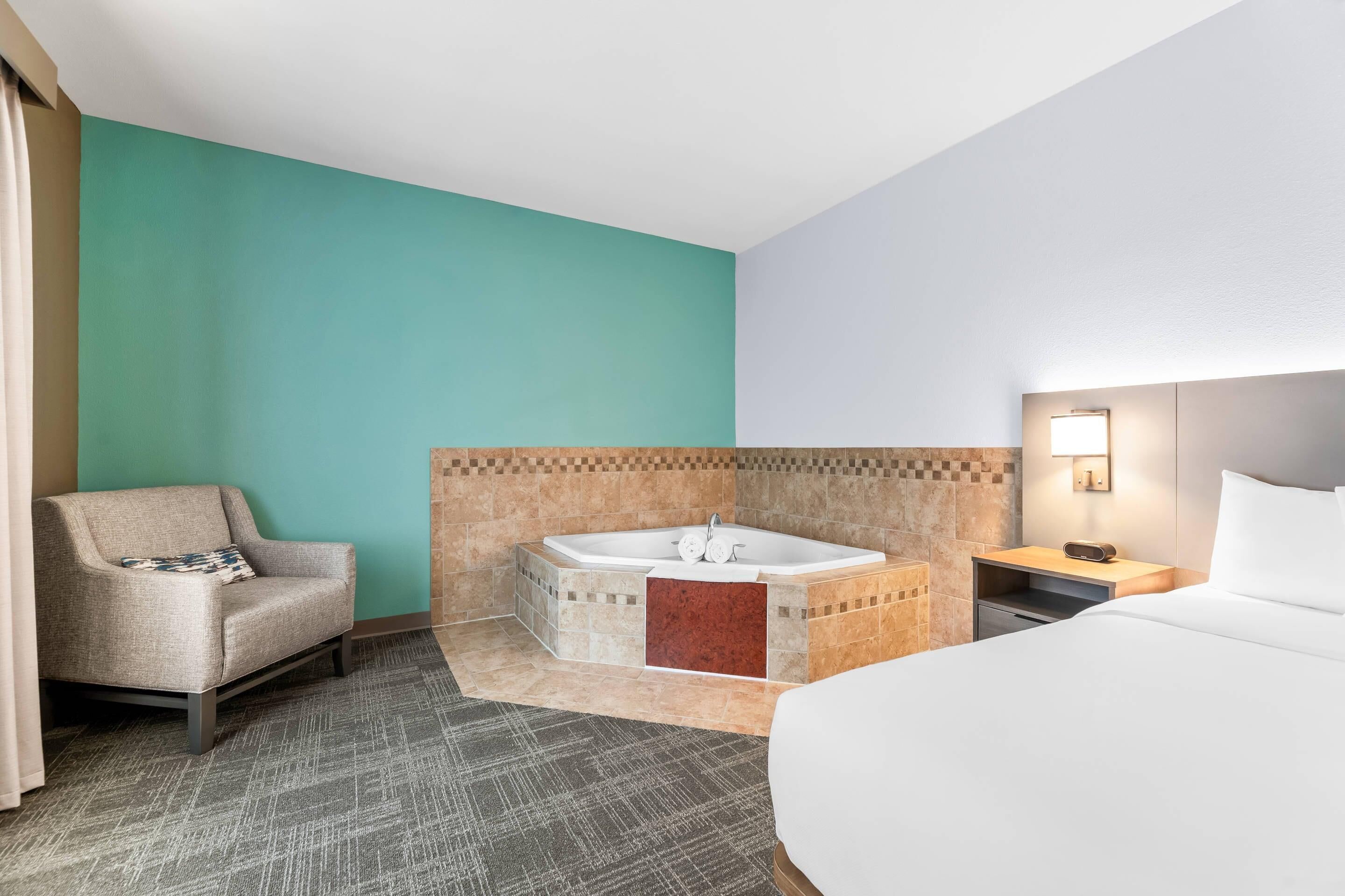 Une chambre d’hôtel avec un lit, une chaise, une baignoire et une table de chevet avec une lampe.