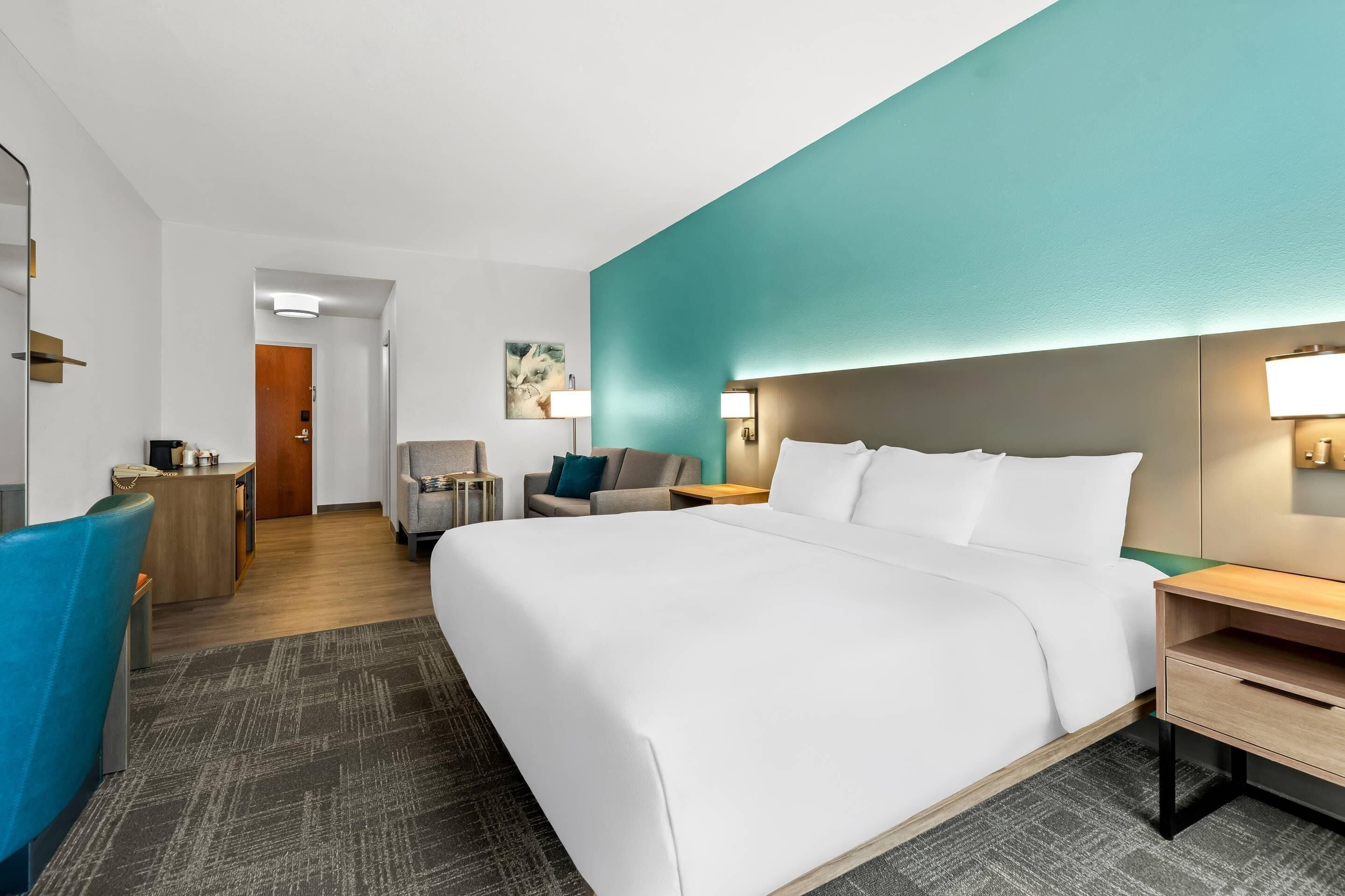 A hotel room with a large bed, a desk, a chair, and a small seating area.