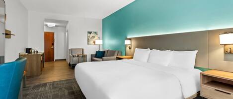 A hotel room with a large bed, a desk, a chair, and a small seating area.