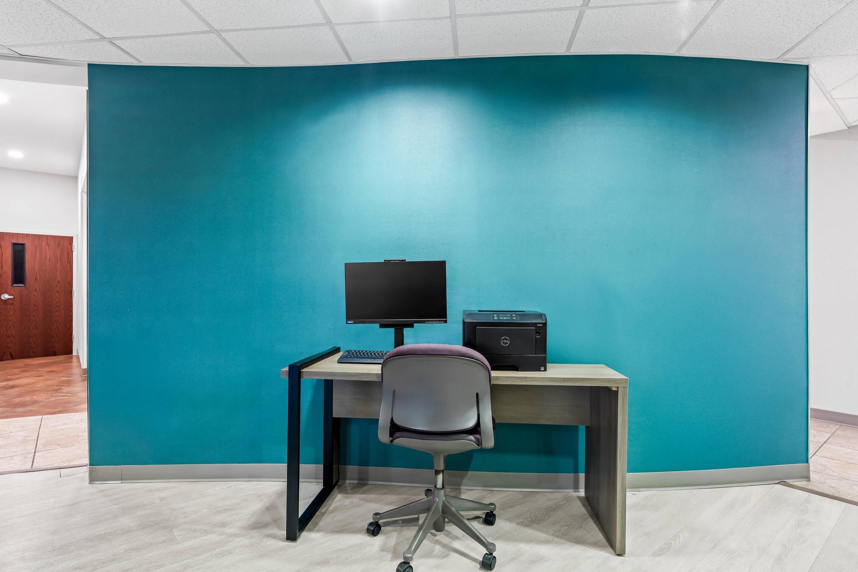 Un espace de bureau moderne avec un mur d’accent de couleur turquoise, un bureau avec un ordinateur et une chaise.