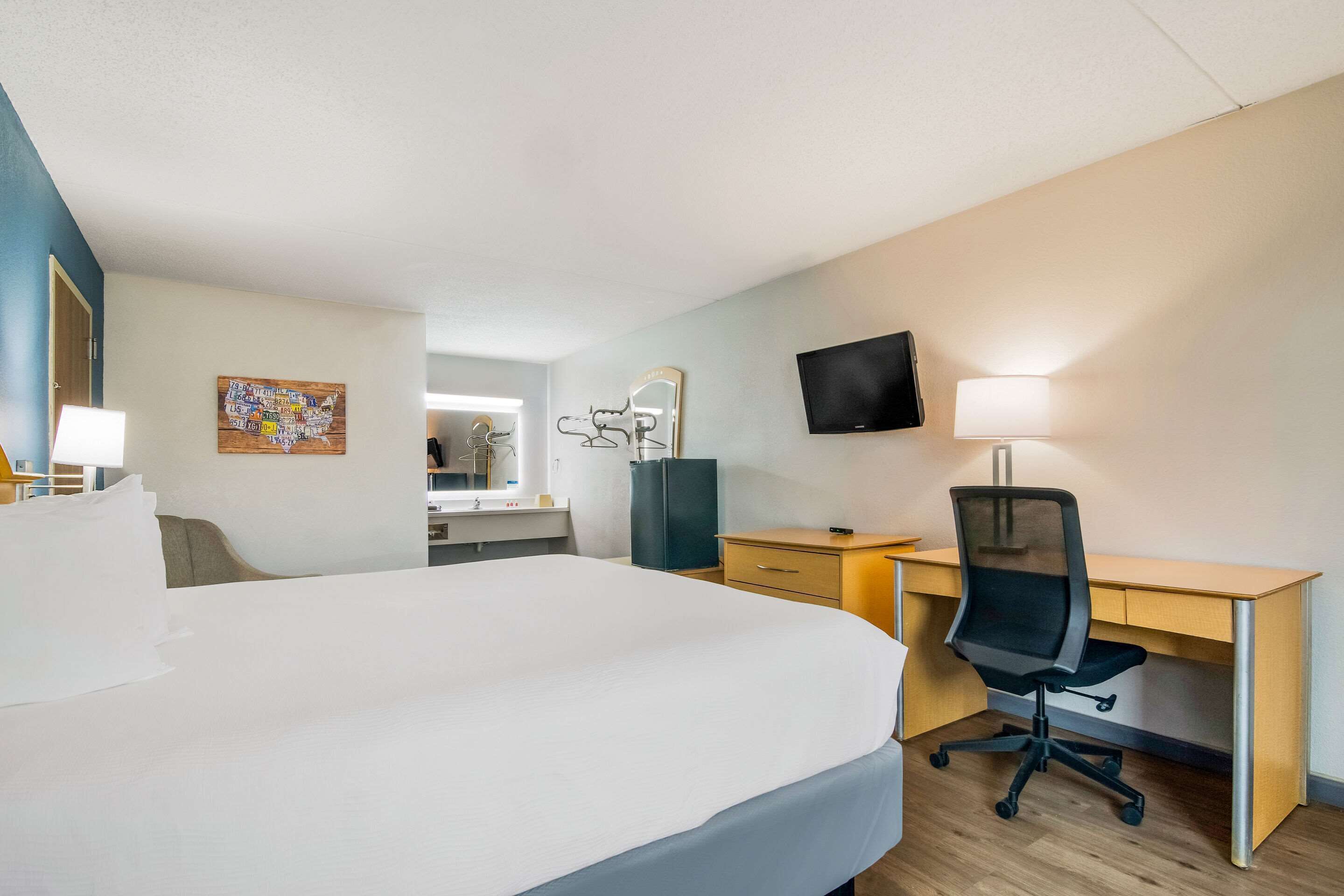 Hotellihuone, jossa on suuri sänky, työpöytä tuolilla, televisio ja seinälle kiinnitetty peili.