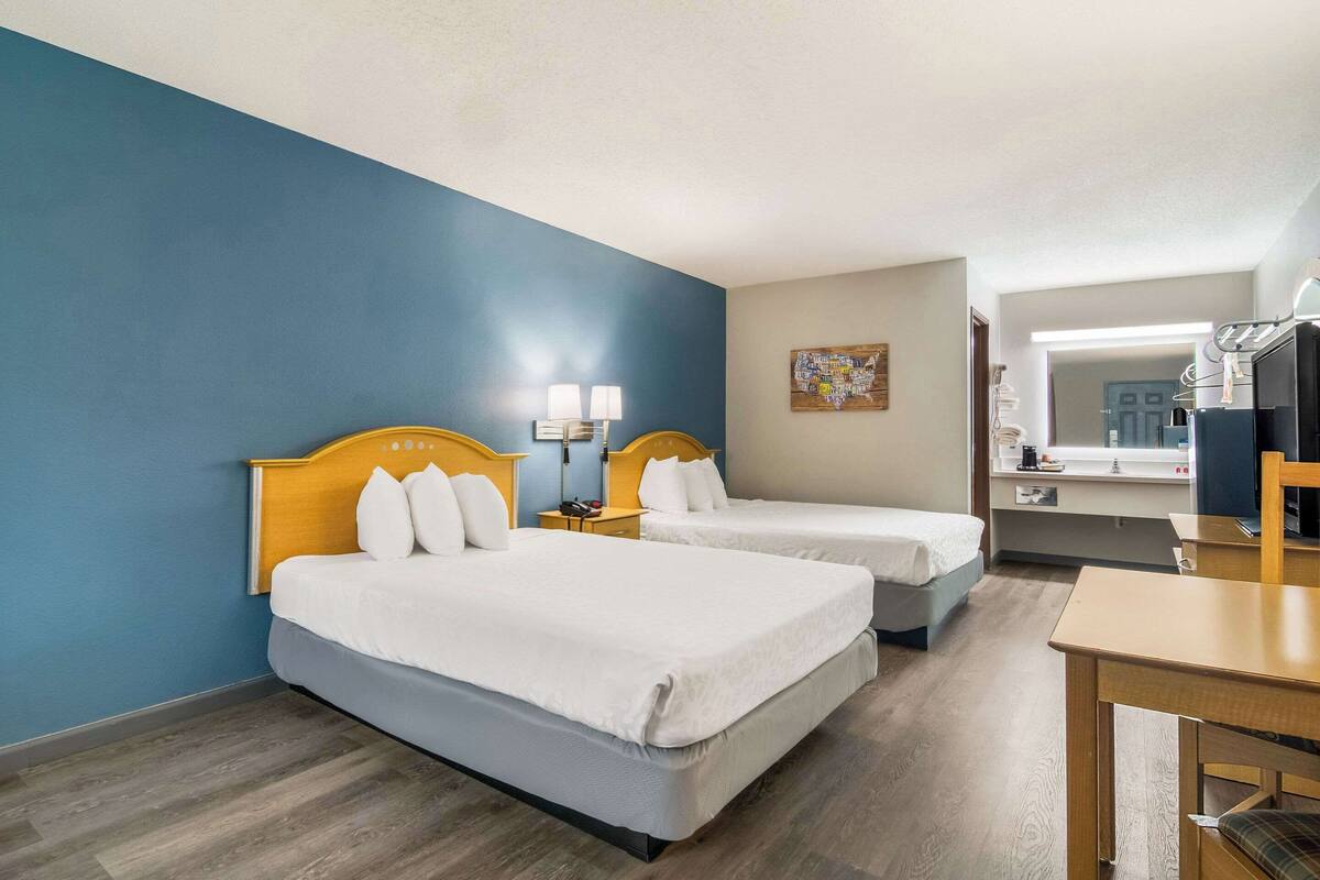 A hotel room with two beds, a desk, a chair, and a bathroom visible through an open door.