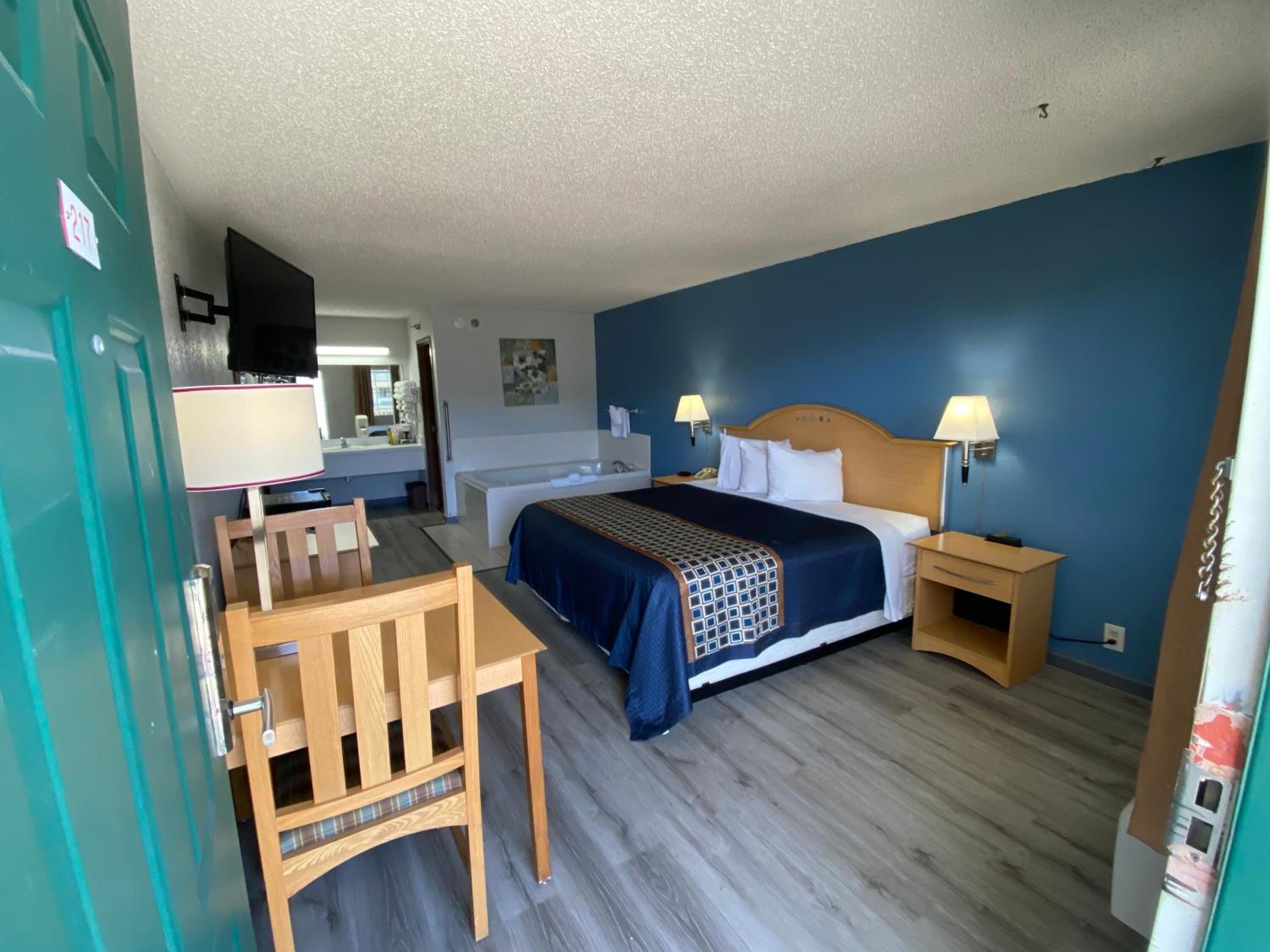 Habitación de hotel con cama, mesitas de noche, escritorio con silla, televisor y baño a la vista.