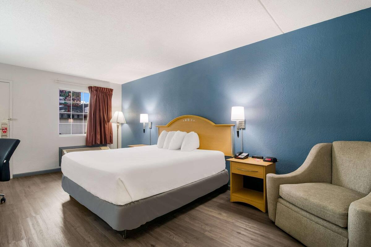 A hotel room with a bed, a desk, a chair, and a window with curtains.