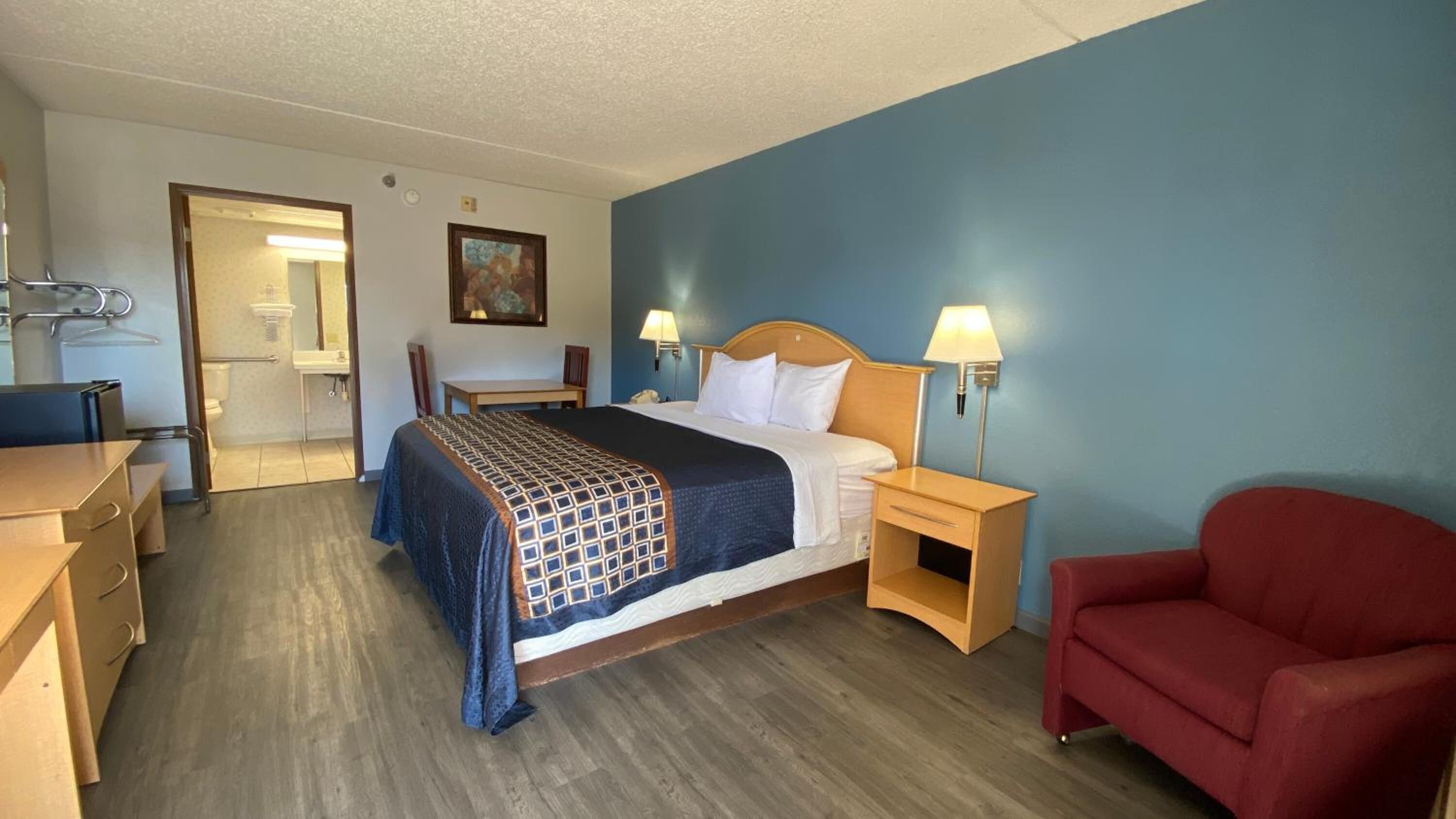 Una habitación de hotel con cama, mesitas de noche, escritorio, silla y un sillón rojo.
