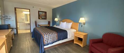 Una habitación de hotel con cama, mesitas de noche, escritorio, silla y un sillón rojo.