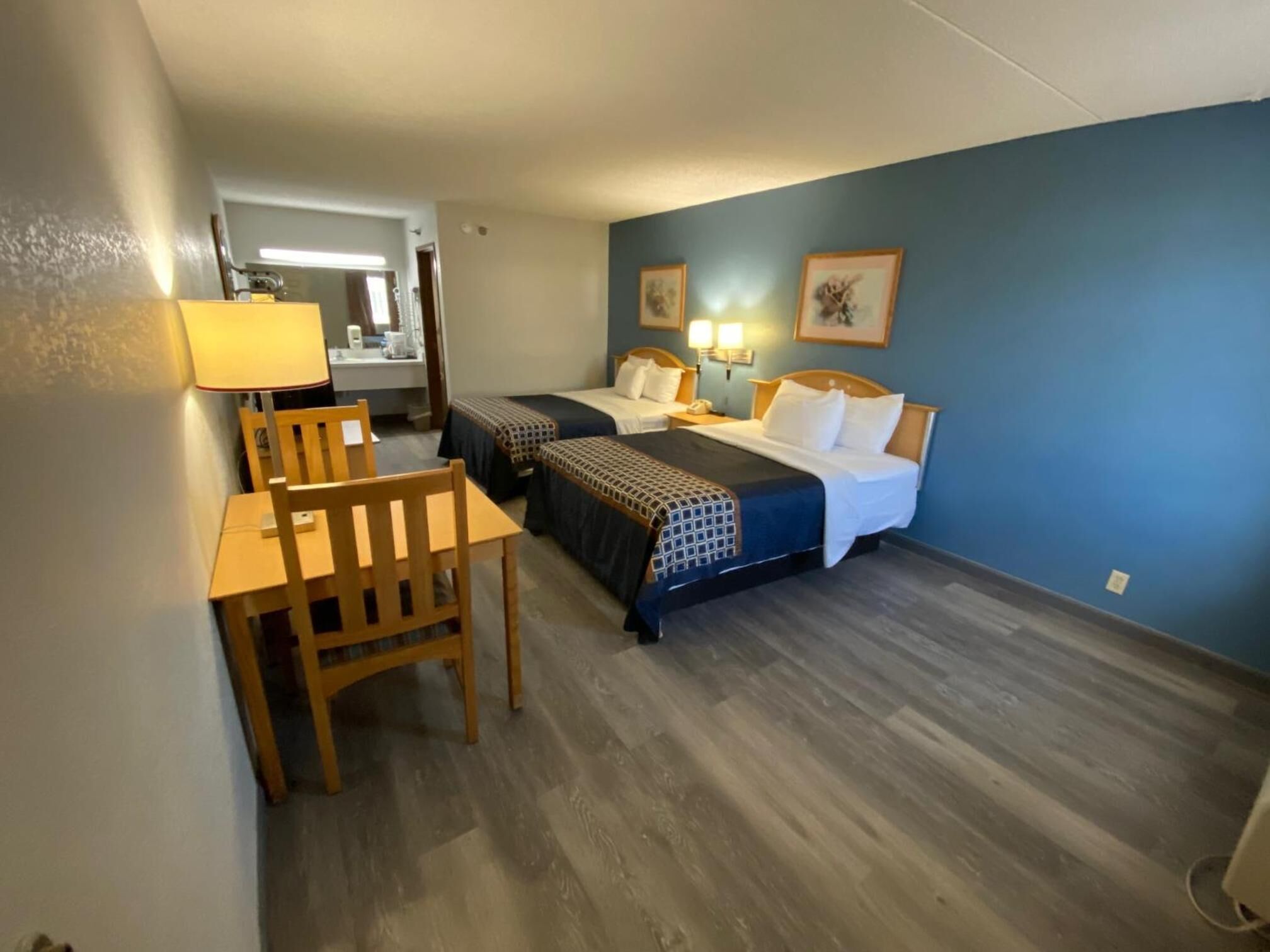 Habitación de hotel con dos camas, un escritorio y una silla. Se ve un baño al fondo.