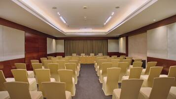 A conference room with rows of chairs, a long table, and a projector screen.