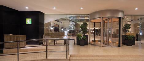 Een moderne hotellobby met een receptiebalie, een draaideur en een trap naar een verdieping erboven.