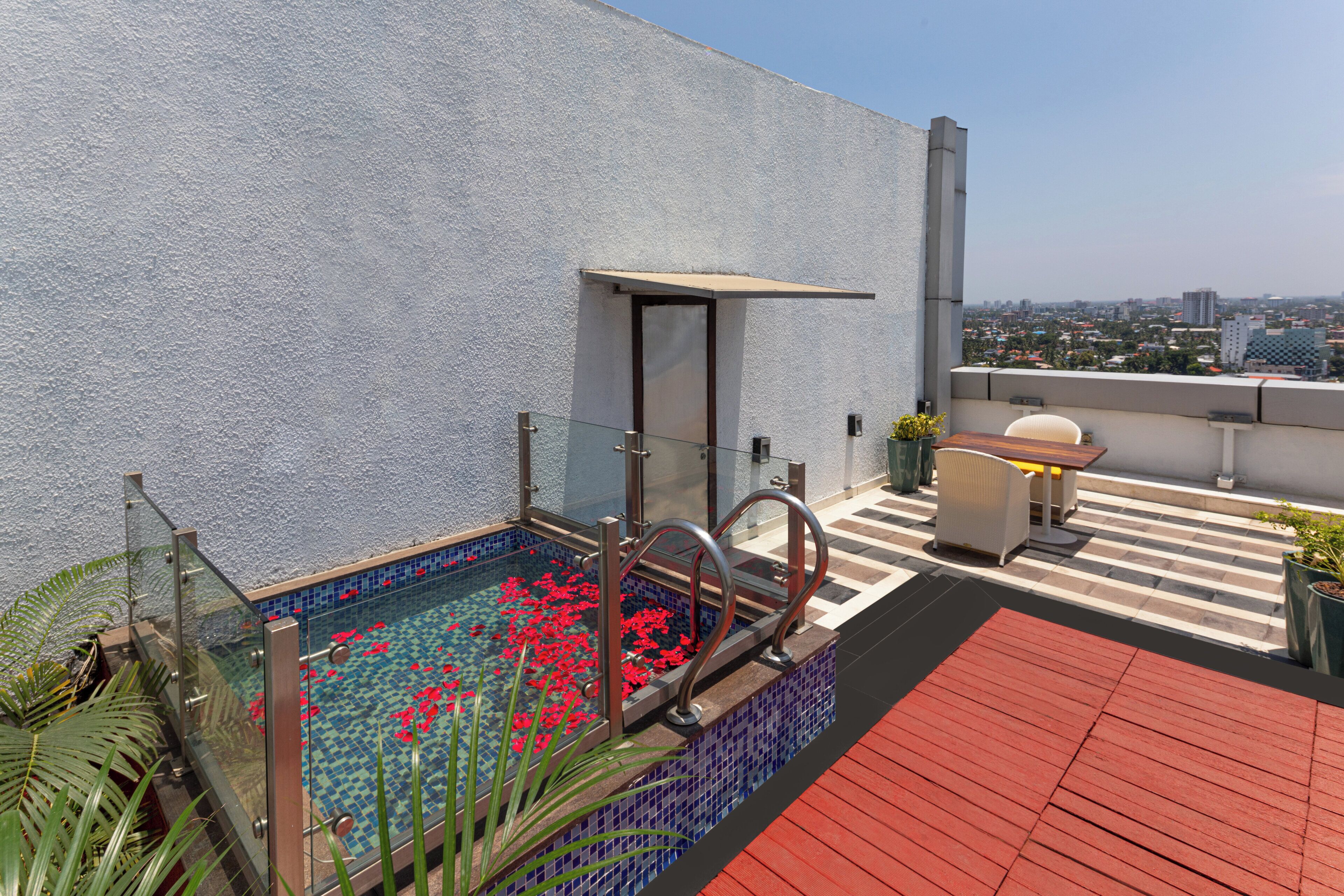 A rooftop pool with a glass enclosure, red flowers, and a red deck.
