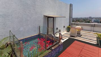 A rooftop pool with a glass enclosure, red flowers, and a red deck.