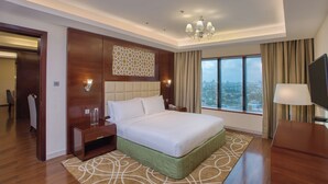 A hotel room with a large bed, a TV, a desk, and a view of the city.