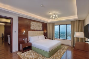 A hotel room with a large bed, a TV, a desk, and a view of the city.