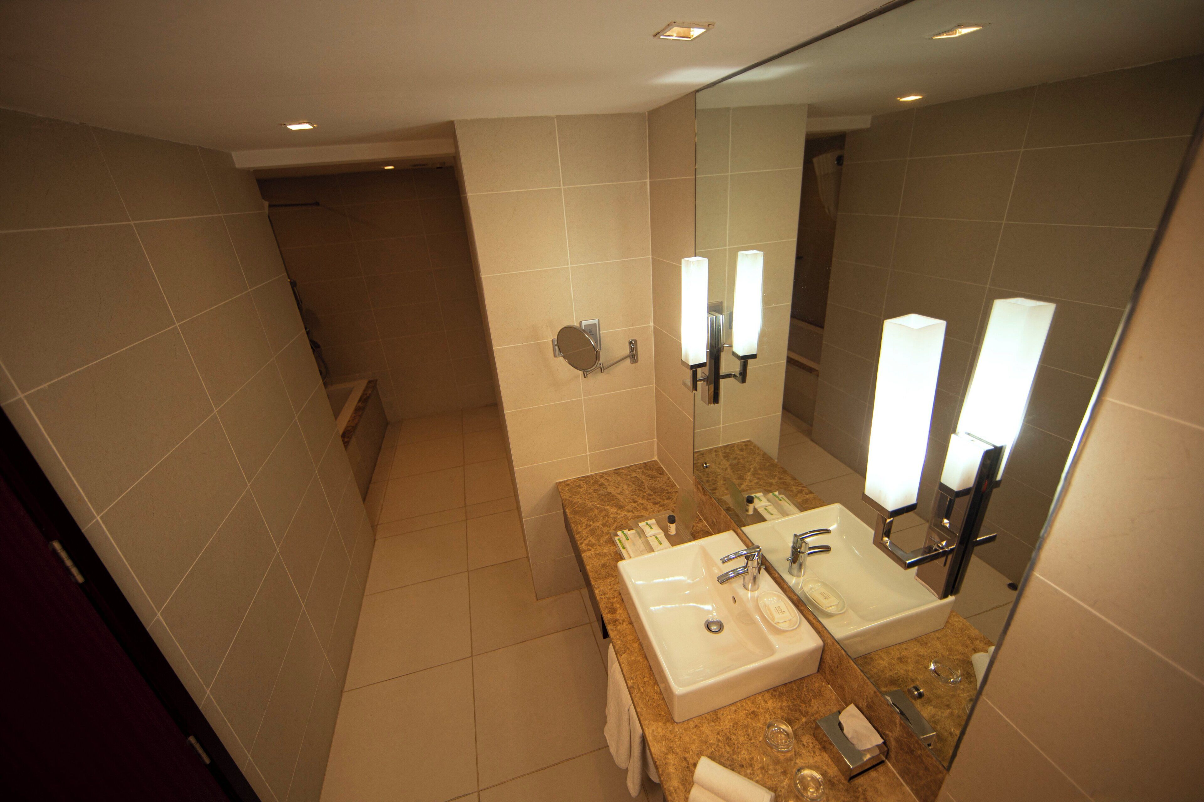 A modern bathroom with a large mirror, two sinks, and a shower area.