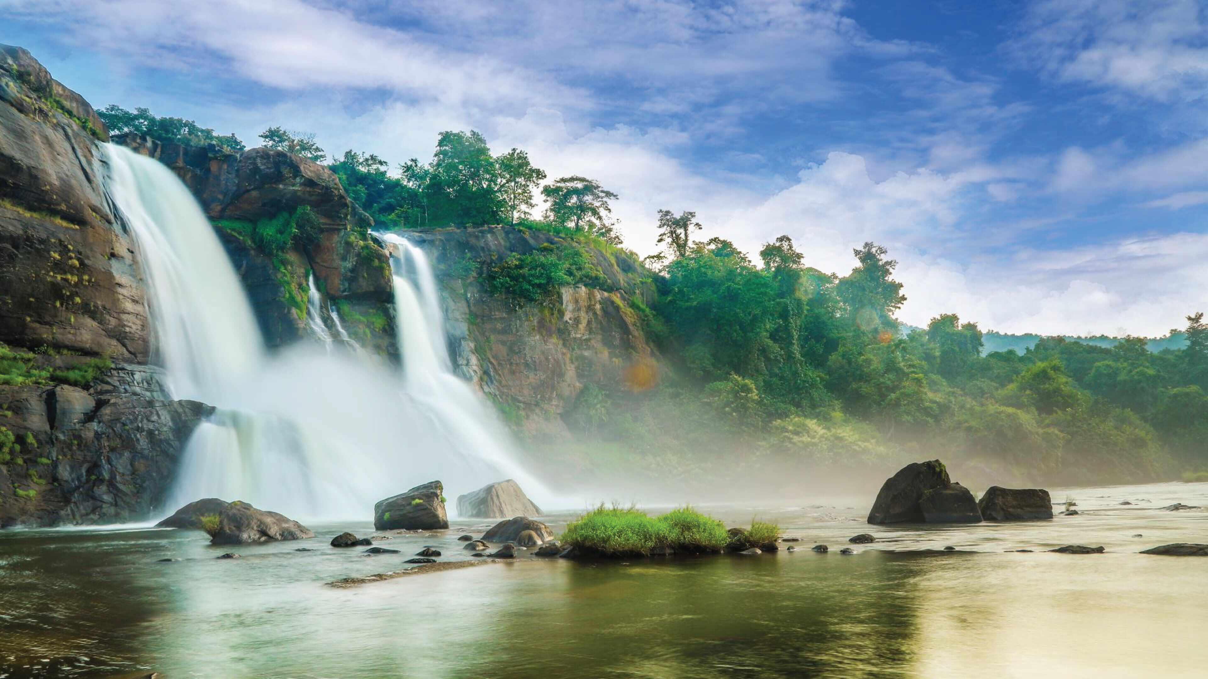 Uma cascata com um rio em primeiro plano, rodeada por rochas e vegetação.