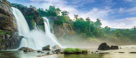 Uma cascata com um rio em primeiro plano, rodeada por rochas e vegetação.