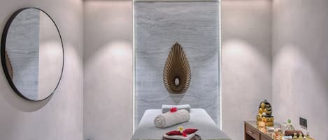 Ein moderner Wellnessraum mit Massageliege, Wanddekoration und einer kleinen Holzeinrichtung mit Gegenständen darauf.