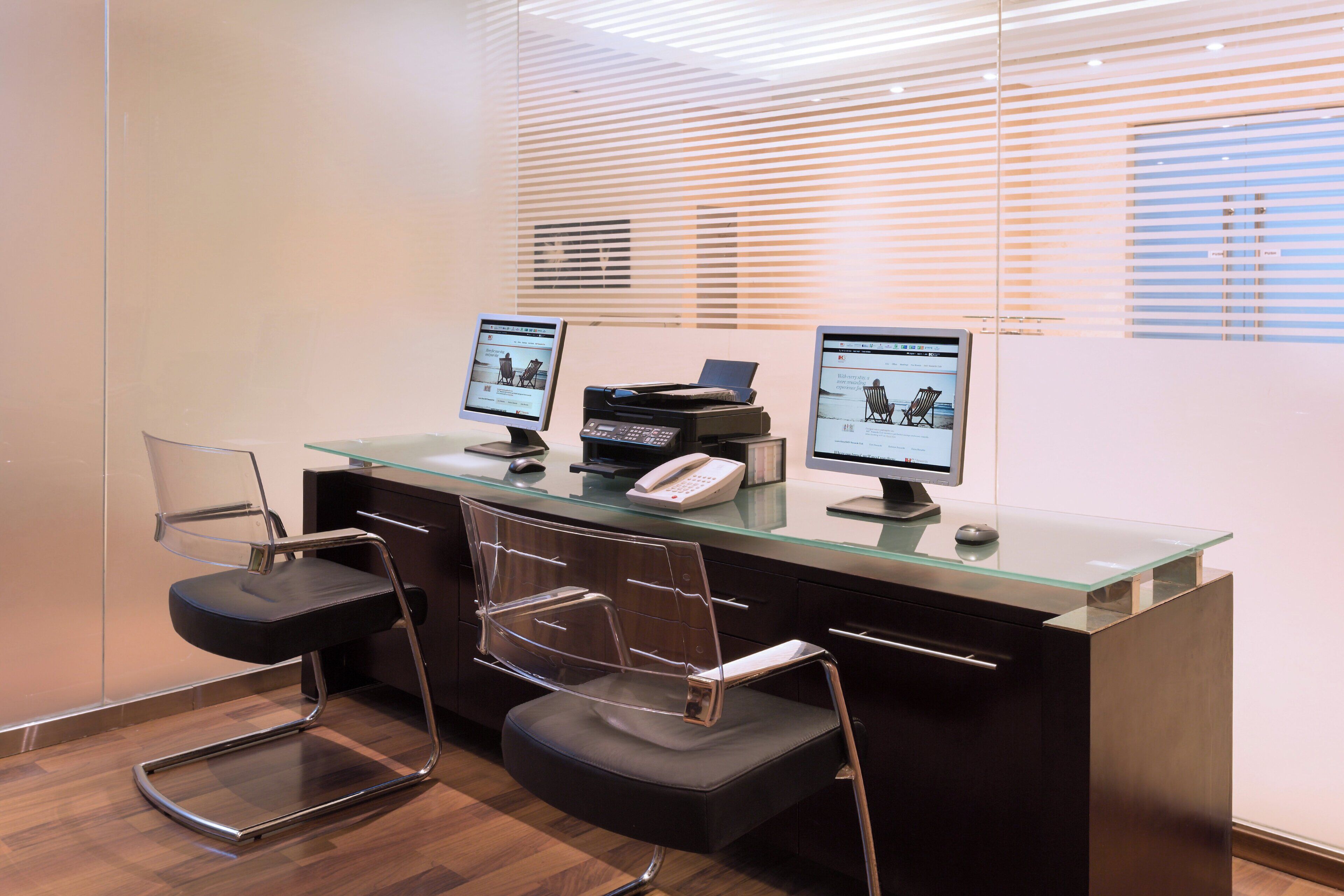 A reception desk with two computer monitors, a telephone, and two modern chairs.