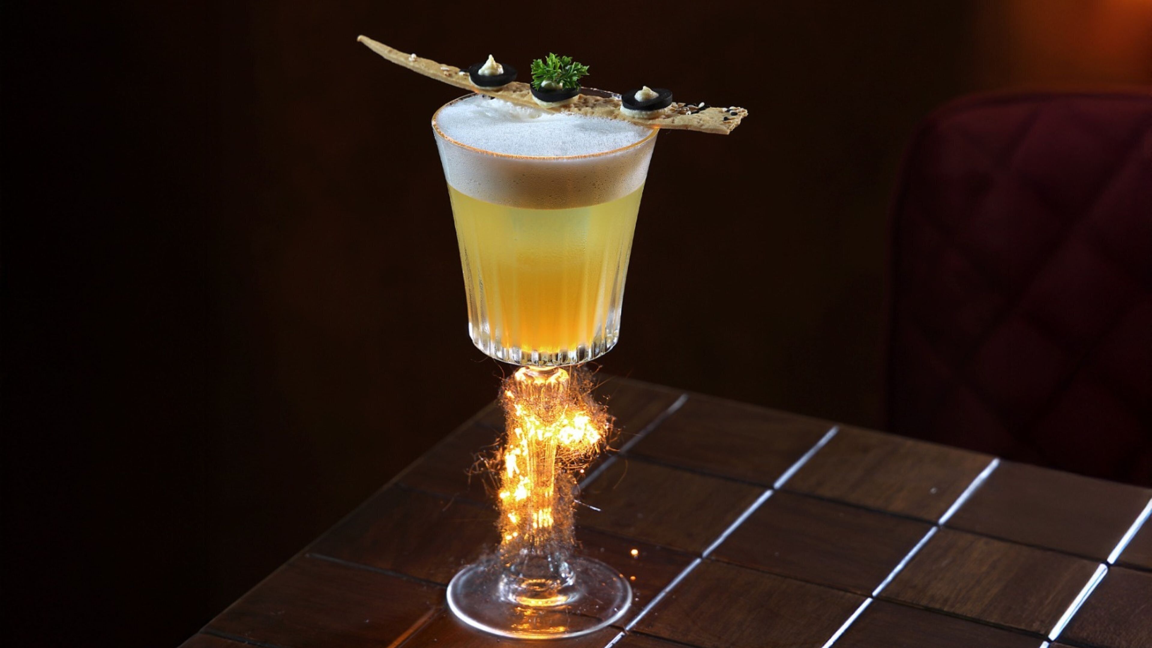 A cocktail with a flaming base on a wooden table.