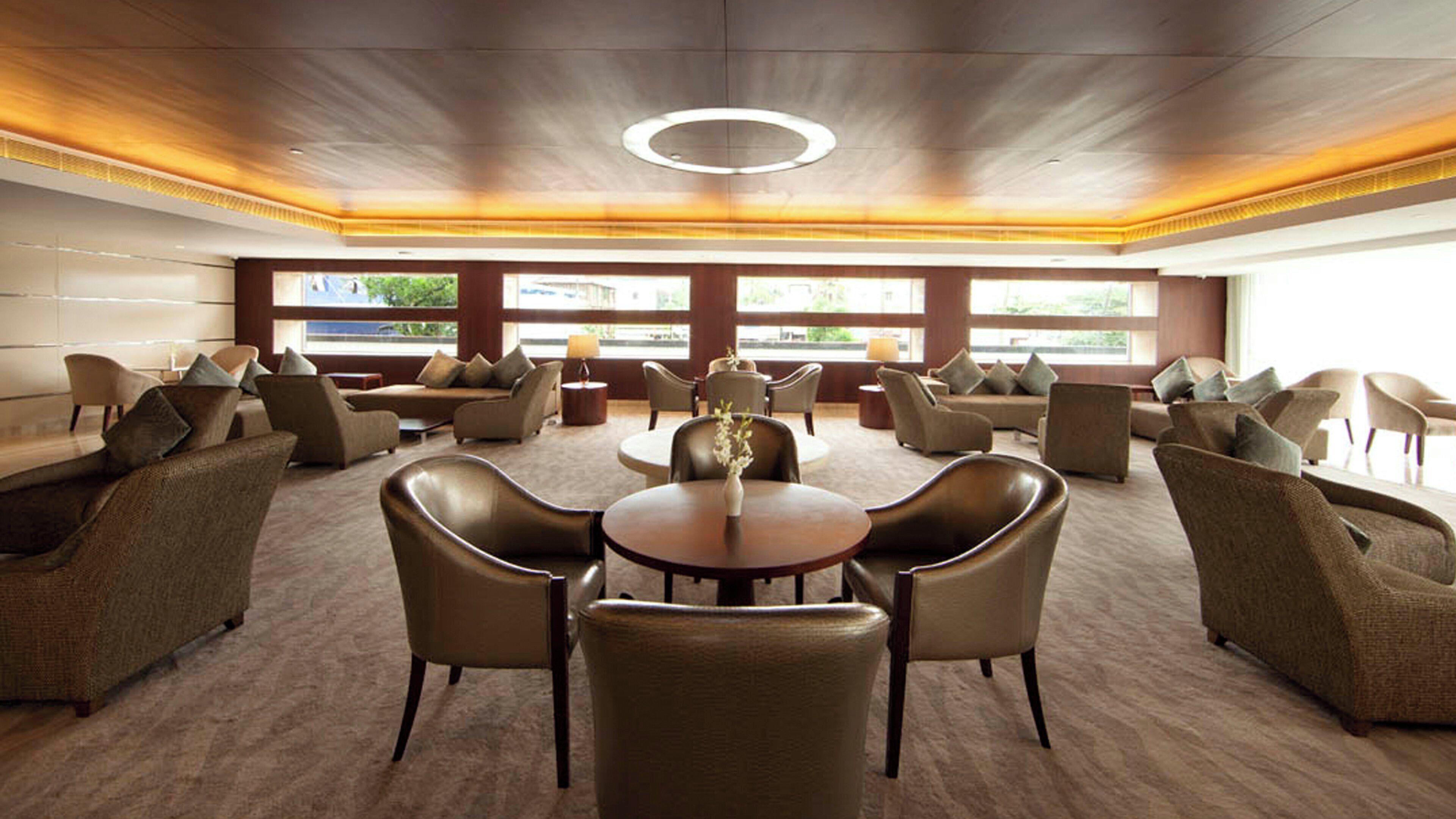 A spacious conference room with a round table, multiple chairs, and large windows providing natural light.