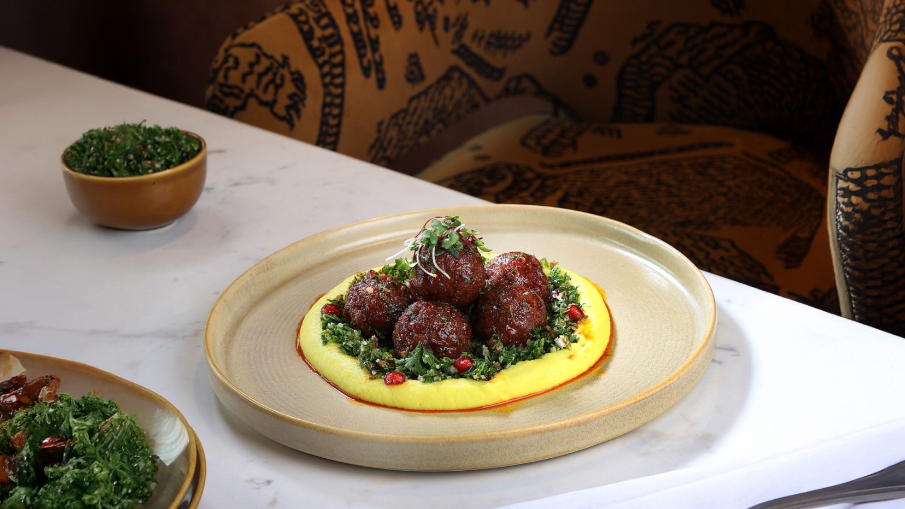 A plate of food with meatballs, greens, and a yellow puree on a ceramic plate.