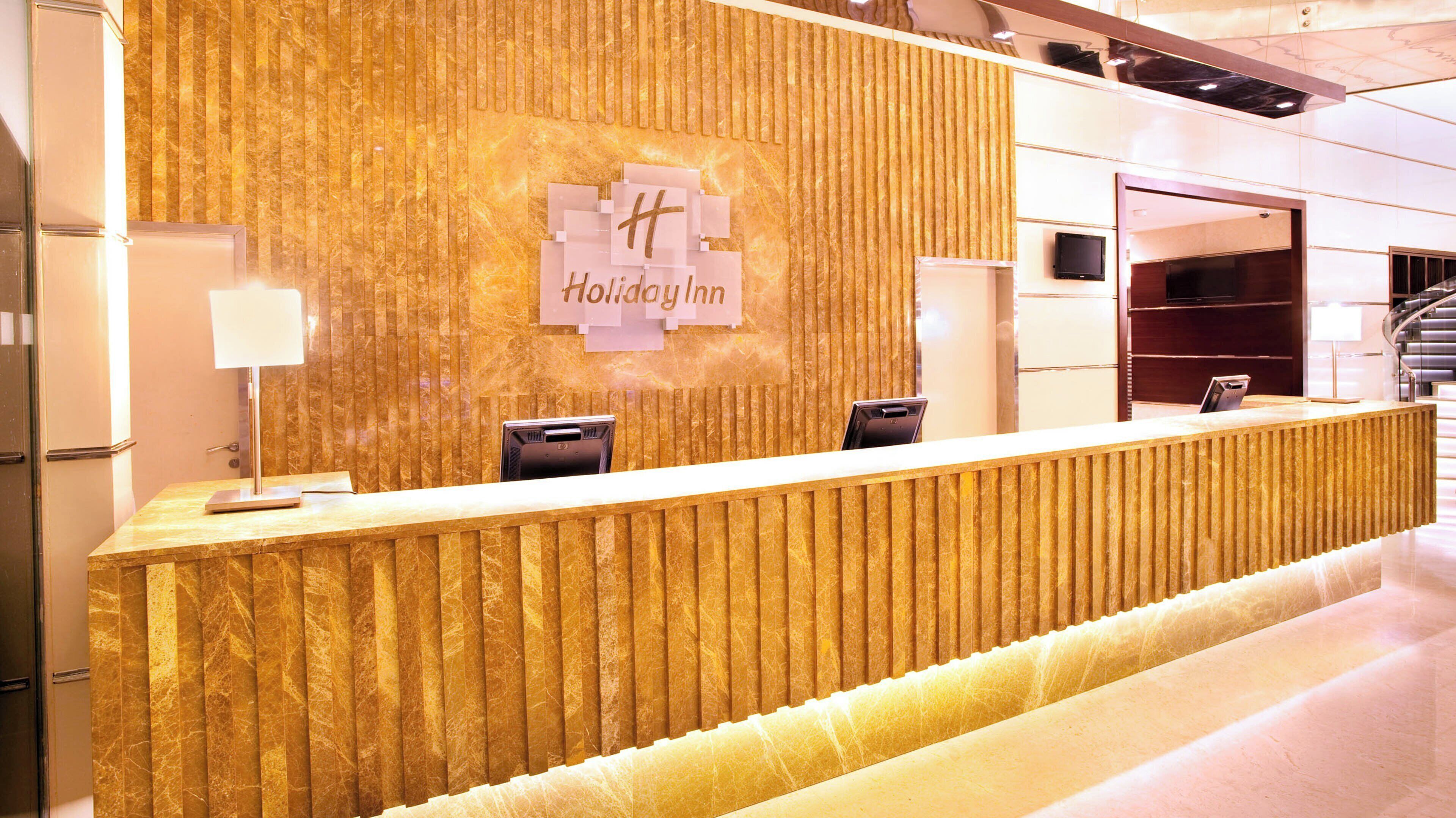 Een receptiebalie met een marmerlook, een wandtelevisie en een bord met de tekst 'Holiday Inn'.